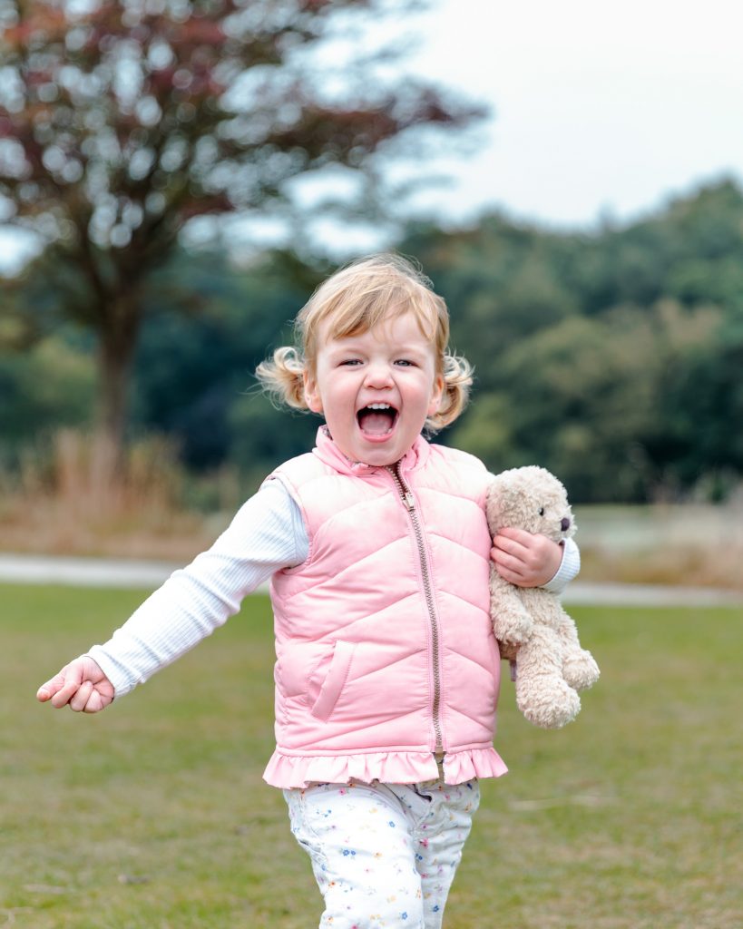 Joyful Toddler holds teddy bear during Mini Portraits Session at Roundhay Park, Leeds.